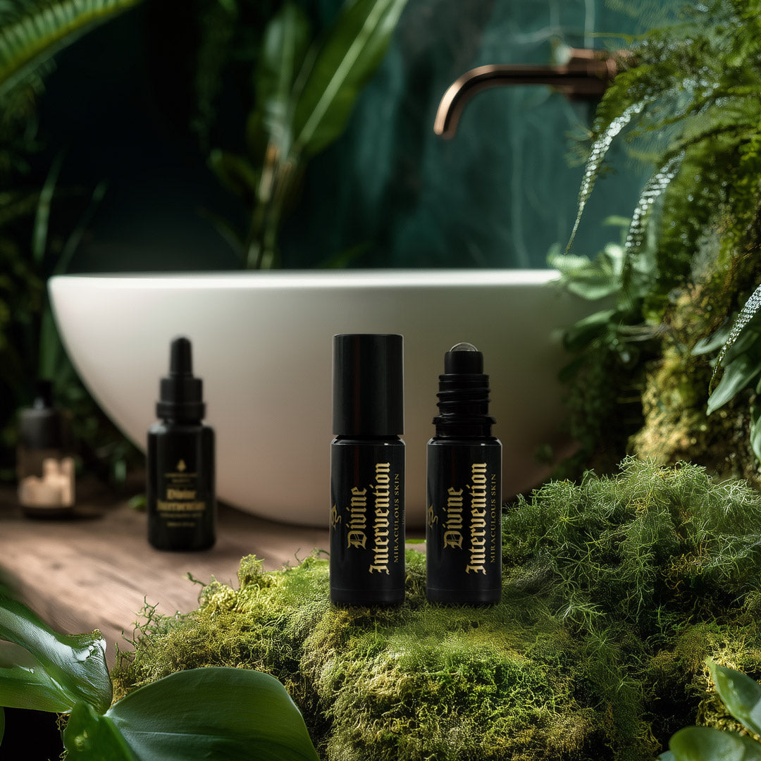 Three black bottles labeled 'Divine Intervention' on a mossy surface with a blurred bathroom sink and plants in the background.