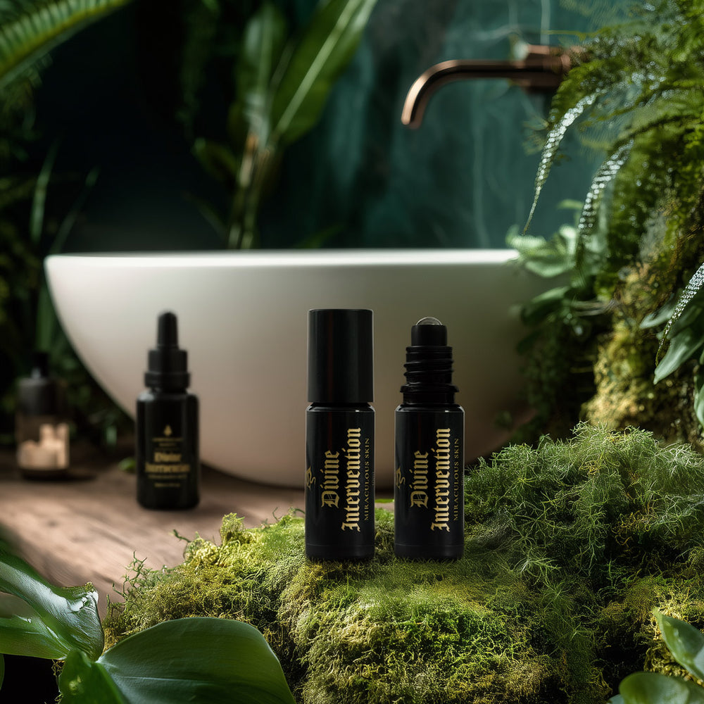 Three black bottles labeled 'Divine Intervention' on a mossy surface with a blurred bathroom sink and plants in the background.