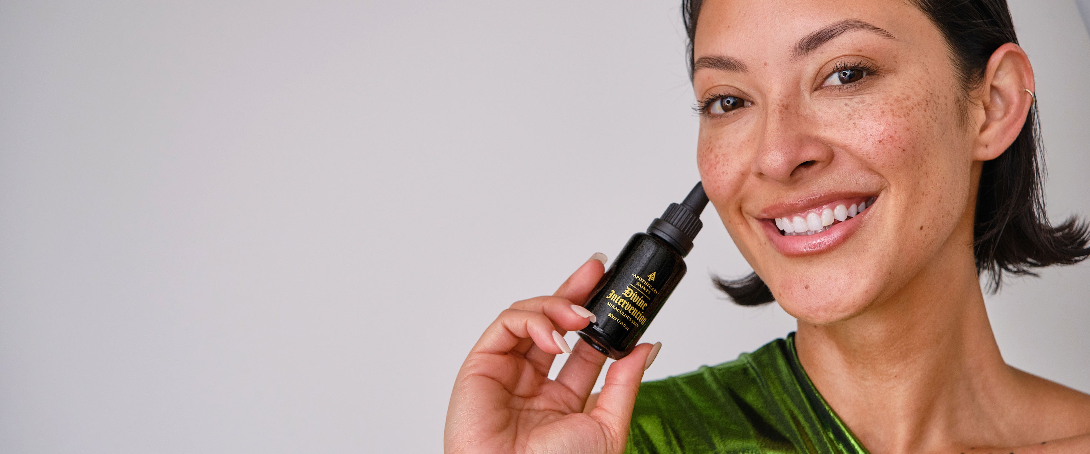 Woman holding a dropper bottle of Divine Intervention face oil with a neutral background