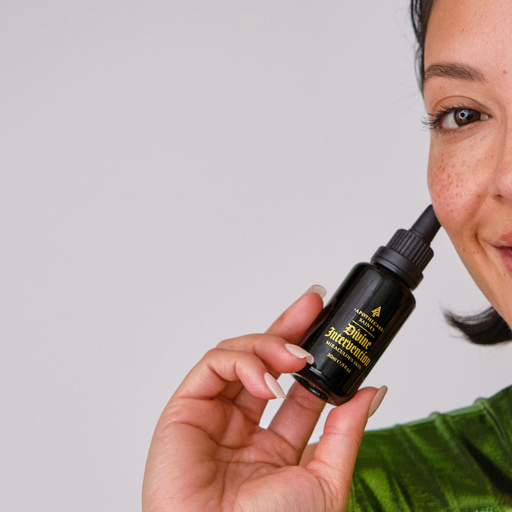 Woman holding a dropper bottle of Divine Intervention face oil with a neutral background