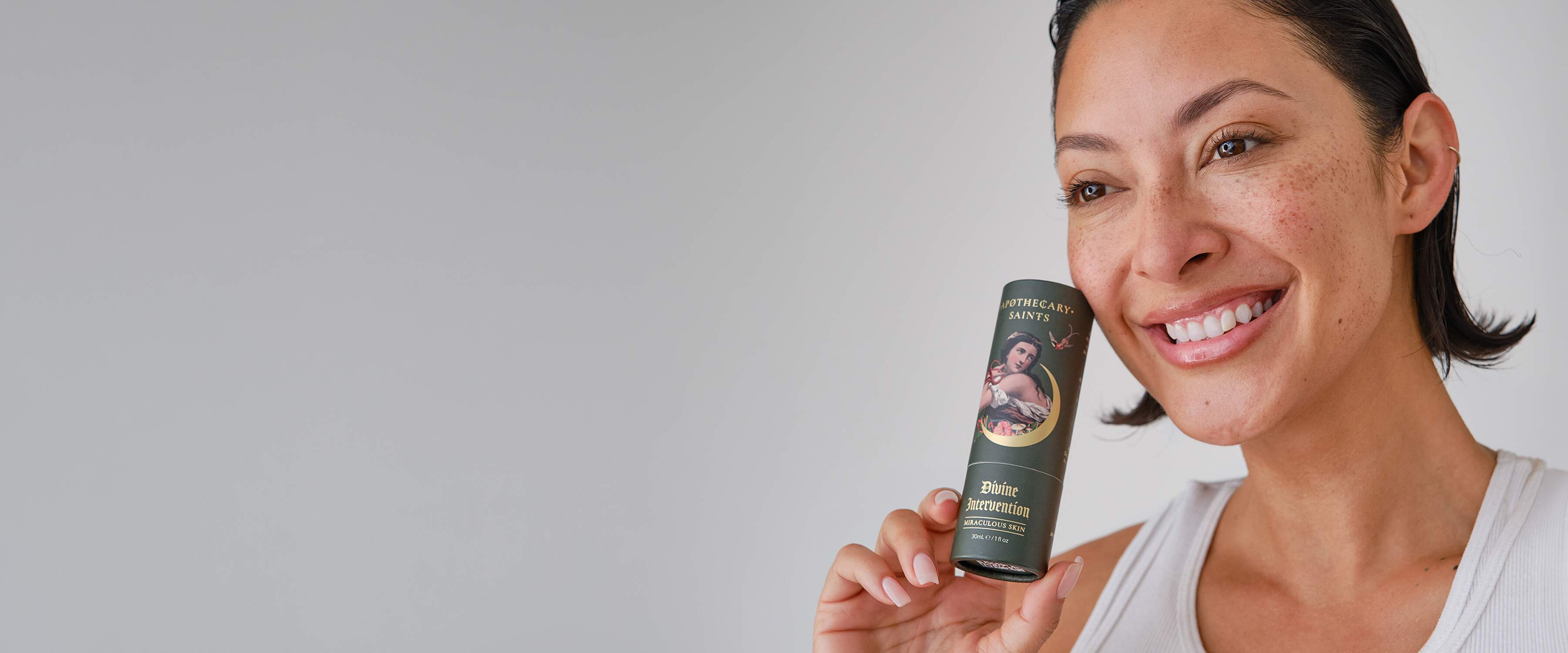 Woman holding Divine Intervention  skincare product with a neutral background