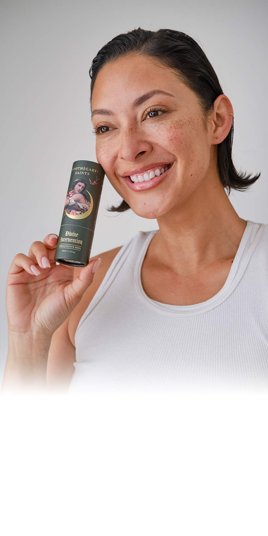 Smiling woman holding Divine Intervention face oil against a white background